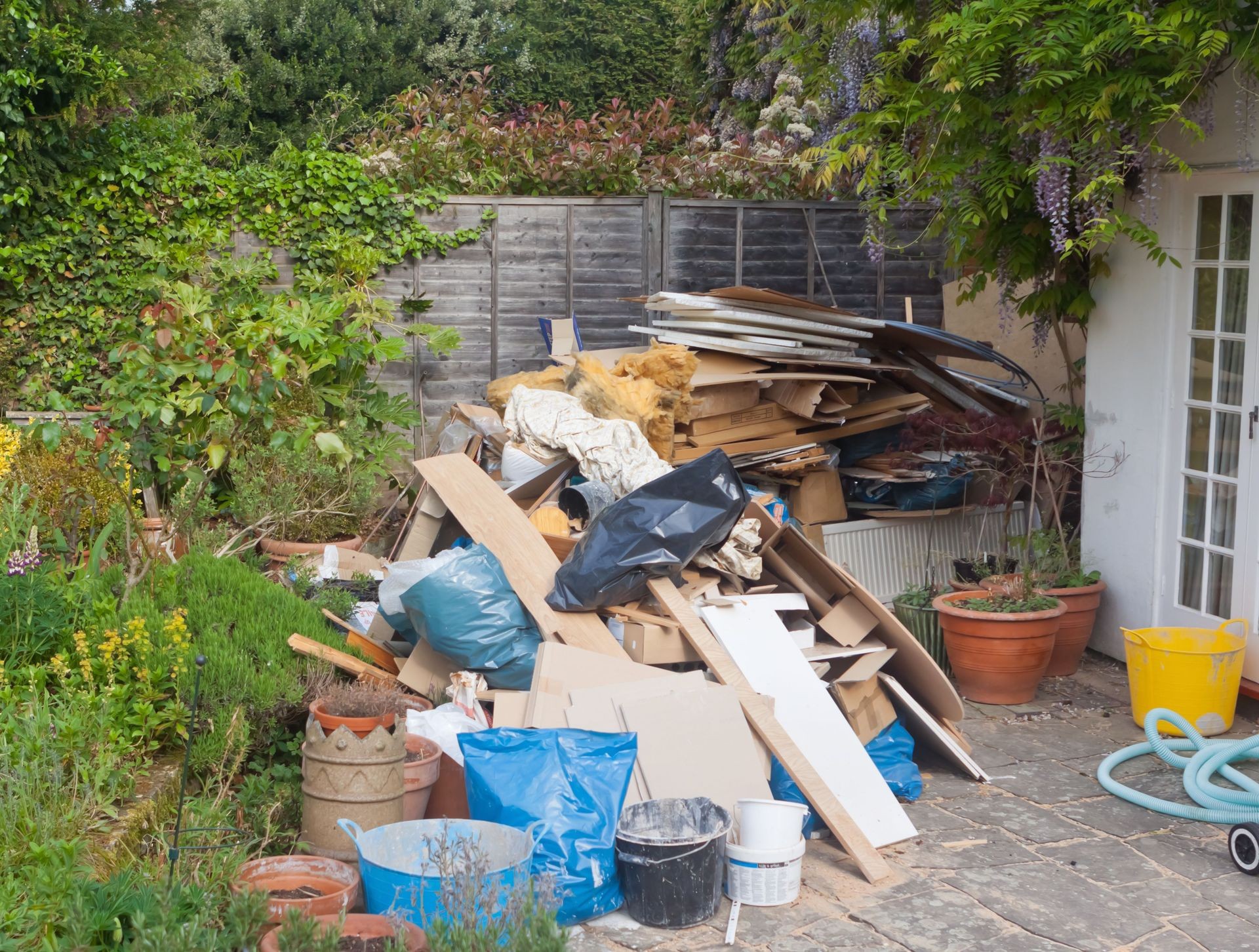 Backyard with a large pile of construction debris and plant pots next to a house wall.